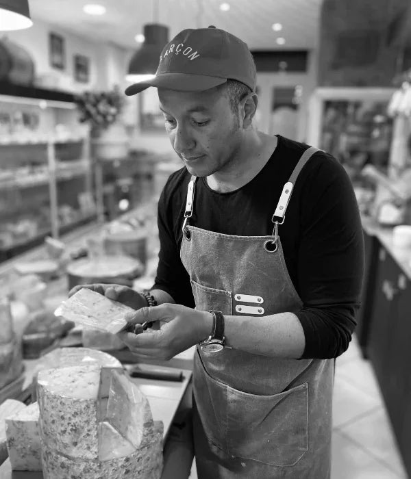 Fromager en tablier examinant un fromage artisanal dans une fromagerie