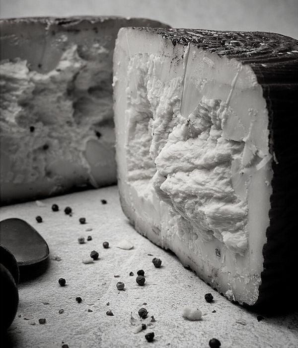Morceau de fromage artisanal affiné à pâte blanche, grains de poivre sur table.